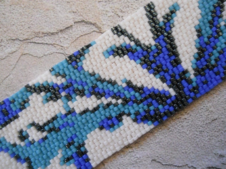 May include: A close-up of a beaded bracelet with a geometric pattern in white, blue, and black.