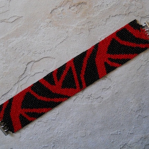 Op de afbeelding: Een zwarte en rode kralen armband met een geometrisch patroon. De armband heeft zilveren metalen sluitingen.