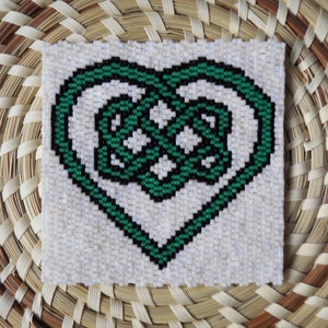 May include: A white beaded heart-shaped design with a green and black Celtic knot pattern.