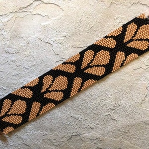 May include: A black and gold beaded bracelet with a geometric pattern. The bracelet is made with small, round beads and has a clasp closure.