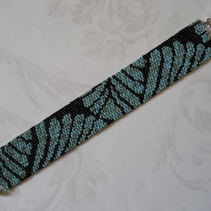 May include: A black and turquoise beaded bracelet with a silver clasp. The bracelet features a geometric pattern.