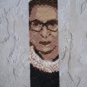 May include: A beaded portrait of a person wearing glasses and a white collar. The portrait is made with brown, black, and white beads.