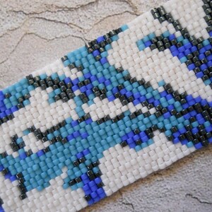 May include: A close-up of a beaded bracelet with a geometric pattern in shades of blue, white, and black.