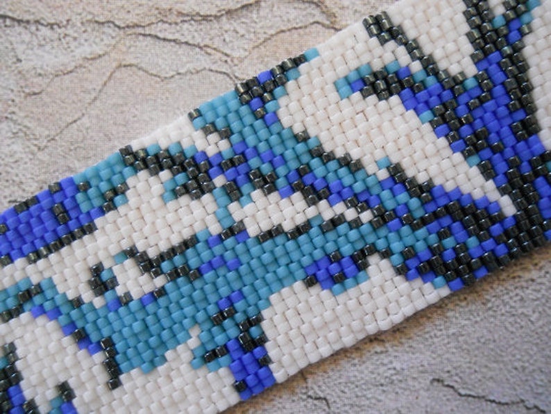 May include: A close-up of a beaded bracelet with a geometric pattern in shades of blue, white, and black.