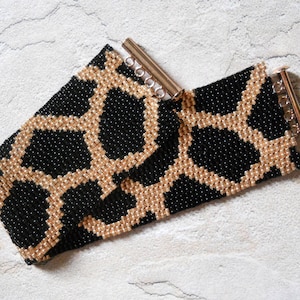 May include: A black and gold beaded bracelet with a geometric pattern. The bracelet has a clasp closure.