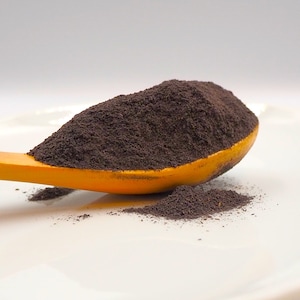 Pode incluir: Uma colher amarela cheia de pó castanho escuro, com uma pequena quantidade de pó derramado num prato branco.
