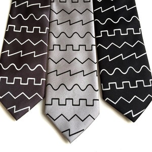May include: Three silk ties with geometric patterns in black, gray, and white. The patterns are a combination of wavy lines and zigzags.