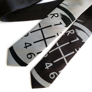 May include: Two neckties with a silver and black herringbone pattern. One tie features a silver gear shift pattern with black numbers, the other tie features a black gear shift pattern with silver numbers.