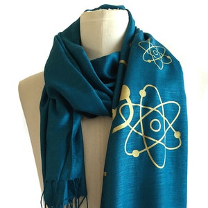 May include: Teal blue scarf with gold atom designs. The scarf has fringe on the ends.