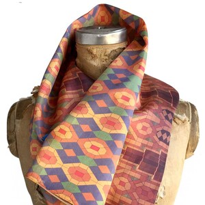 May include: A colorful infinity scarf with a geometric pattern in shades of orange, purple, green, and red. The scarf is draped over a vintage mannequin, showcasing its design and texture. The pattern includes diamond and oval shapes.