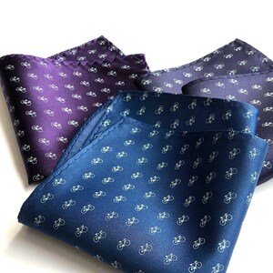 May include: Three pocket squares with a white bicycle pattern on a blue, purple, and dark blue background.