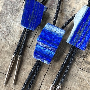 May include: Three bolo ties with blue and white lapis lazuli stone pendants on black braided cords.