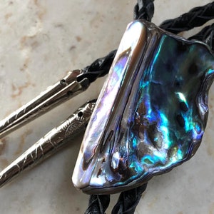 Könnte beinhalten: Ein Bolo-Halsschmuck mit einem großen, schillernden Abalone-Muschel-Anhänger und einer schwarzen Lederschnur.