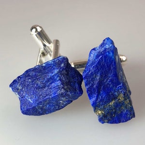 May include: A pair of cufflinks featuring a deep blue lapis lazuli stone. The stones are set in silver and have a polished finish.