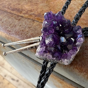 May include: A purple amethyst crystal cluster bolo tie with a silver-toned metal clasp and black braided cord.