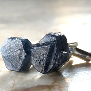 May include: A pair of cufflinks featuring a dark blue, faceted gemstone. The cufflinks are made of silver metal.