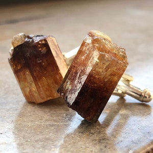 May include: A pair of cufflinks featuring two brown and gold topaz crystals set in silver.