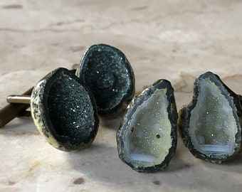 May include: A set of four cufflinks featuring geode stone insets. The cufflinks are made of metal with a dark brown finish. The geode stones are a mix of green, white, and brown.