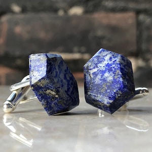 Puede incluir: Un par de gemelos con una piedra de lapislázuli cortada geométricamente. Las piedras son de un azul intenso con motas blancas y doradas.