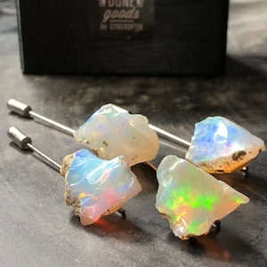 May include: Four iridescent opal stones mounted on silver pins. The opals are a mix of white, blue, green, and orange.