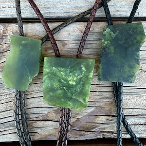 May include: Three bolo ties featuring irregular, flat, polished green stone slabs as centrepieces. Each stone displays unique natural marbling and colour variations. The cords are made of braided leather in dark brown and black tones.