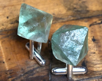 May include: A pair of cufflinks featuring green fluorite crystals set in silver.
