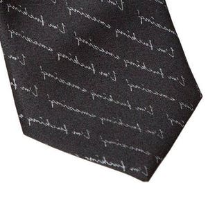 May include: A black silk tie with a white repeating pattern of the text "I'm fucking amazing".