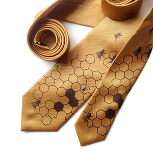 Peut inclure: Une cravate en soie dorée avec un motif en nid d'abeille et des silhouettes d'abeilles noires.