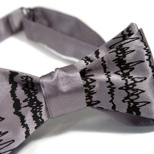 May include: A gray bow tie with a black wavy pattern. The bow tie is made of satin and has a classic shape.