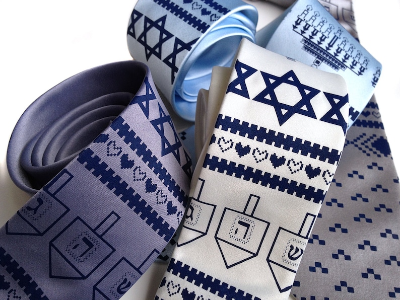 May include: An assortment of neckties in various shades of blue and white, featuring Jewish symbols. The ties display patterns of the Star of David, dreidels, and hearts. The ties are made of a smooth fabric.