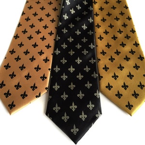 May include: Three silk ties with a fleur-de-lis pattern. One tie is black with silver fleur-de-lis, one is gold with black fleur-de-lis, and one is gold with black fleur-de-lis.