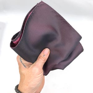 Op de afbeelding: Een gevouwen donkerpaarse zakdoek met een roze satijnen voering.
