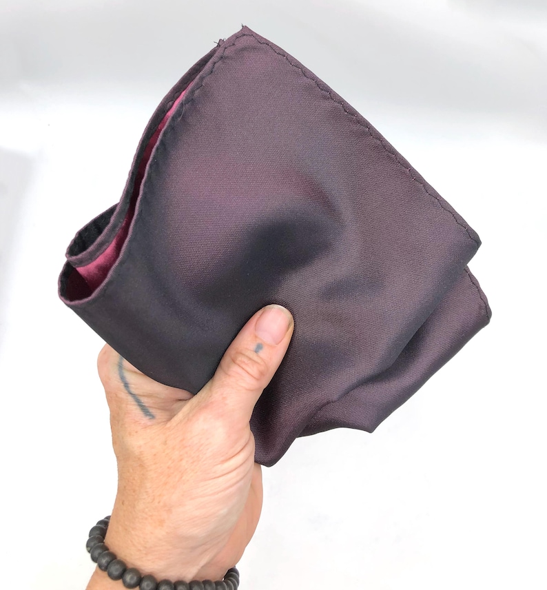 Op de afbeelding: Een gevouwen donkerpaarse zakdoek met een roze satijnen voering.