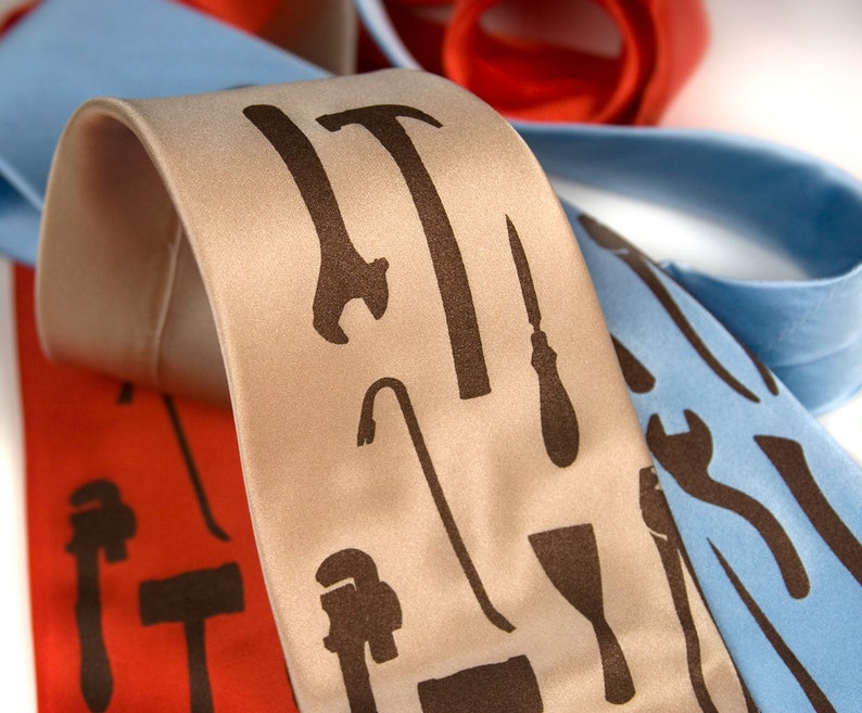 May include: Three neckties with different tool designs. The first tie is light blue with a wrench, hammer, and screwdriver design. The second tie is beige with a hammer, crowbar, screwdriver, and putty knife design. The third tie is red with a wrench, hammer, and screwdriver design.