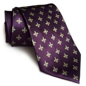 May include: A purple silk tie with a repeating pattern of gold fleur-de-lis.
