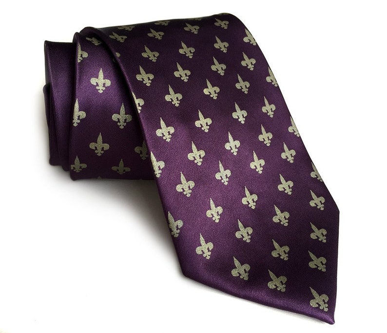 May include: A purple silk tie with a repeating pattern of gold fleur-de-lis.