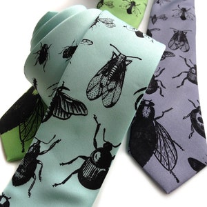 May include: Two silk neckties with insect patterns. One tie is light blue with black insects, the other is gray with black insects.