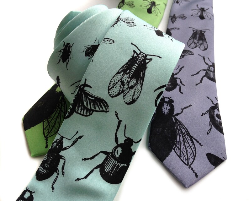May include: Two silk neckties with insect patterns. One tie is light blue with black insects, the other is gray with black insects.