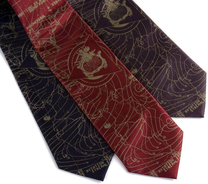 May include: Three silk neckties with a map-like pattern in gold on a dark background. The ties are in burgundy, dark purple, and black. The text on the ties reads "Aviation Streamline 100".
