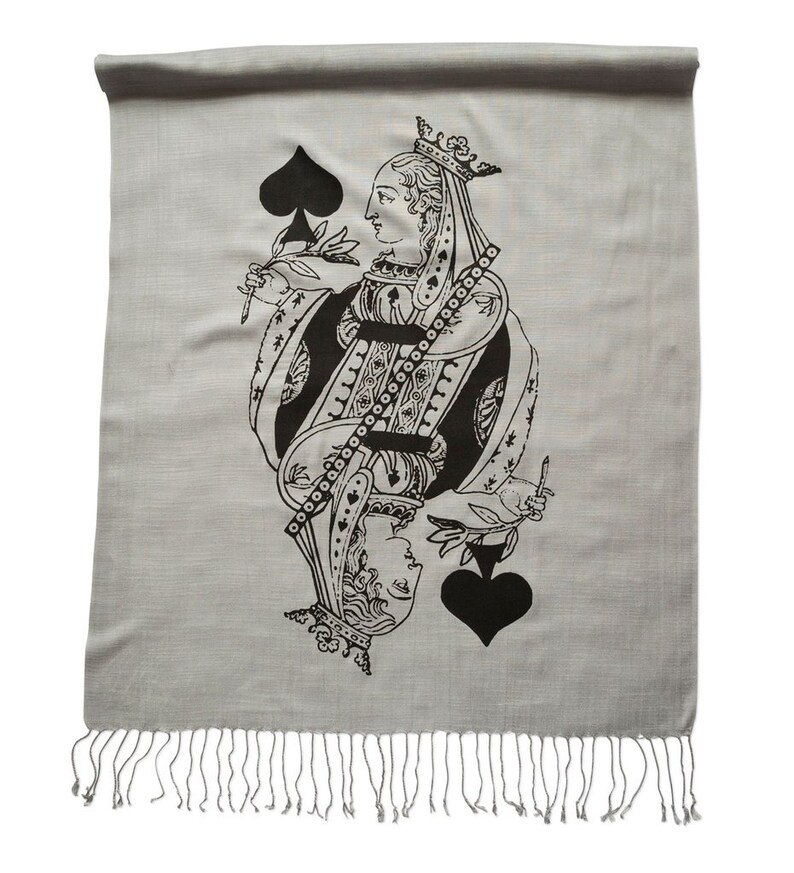 May include: A gray scarf with a black and white image of the Queen of Spades playing card. The scarf has a fringe border.