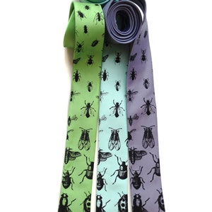 May include: Three silk neckties with a pattern of black insects on a light green, light blue, and purple background.