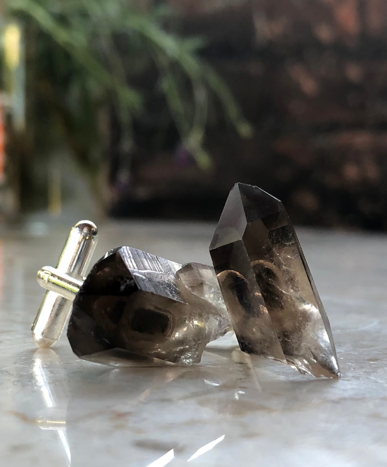 May include: A pair of cufflinks featuring two smoky quartz crystals attached to silver cufflink backs.