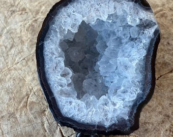 May include: A bolo tie featuring a large, circular geode slice with a dark, polished outer rim and a hollow center filled with sparkling, translucent white quartz crystals, attached to a braided black leather cord with metal tips.