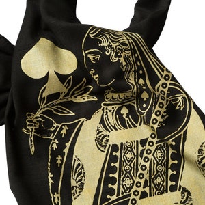 May include: A black fabric tote bag with a gold design of the Queen of Spades playing card. The Queen is holding a flower and wearing a crown.