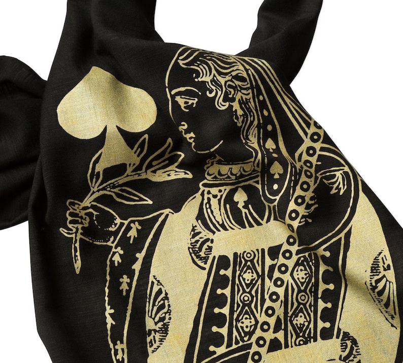 May include: A black fabric tote bag with a gold design of the Queen of Spades playing card. The Queen is holding a flower and wearing a crown.