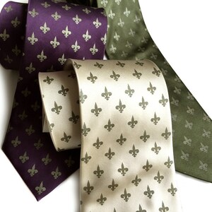 May include: Three silk ties with a fleur-de-lis pattern. One tie is purple, one is green, and one is beige.