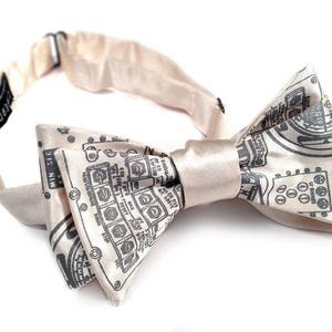 May include: A beige bow tie with a black and white circuit board pattern. The bow tie is made of satin and has a simple design.