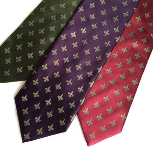 May include: Three silk ties with a repeating pattern of gold fleur-de-lis on a dark green, purple, and red background.