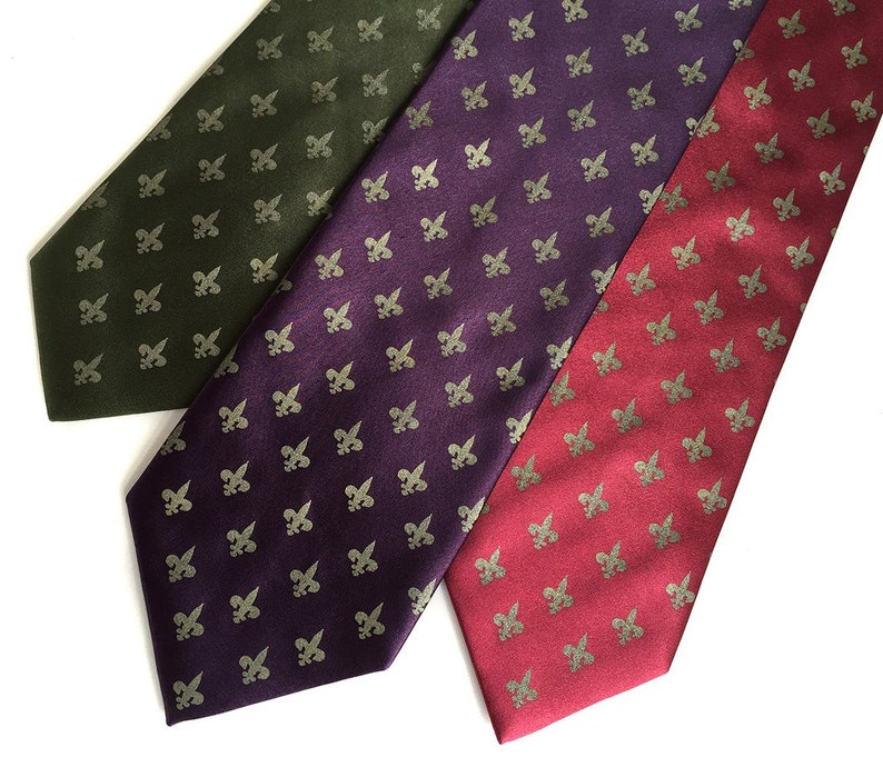 May include: Three silk ties with a repeating pattern of gold fleur-de-lis on a dark green, purple, and red background.