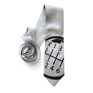 May include: A grey silk tie with a black printed gear shift pattern. The pattern includes the letters R, L, and the numbers 1, 2, 3, 4, 5, and 6.